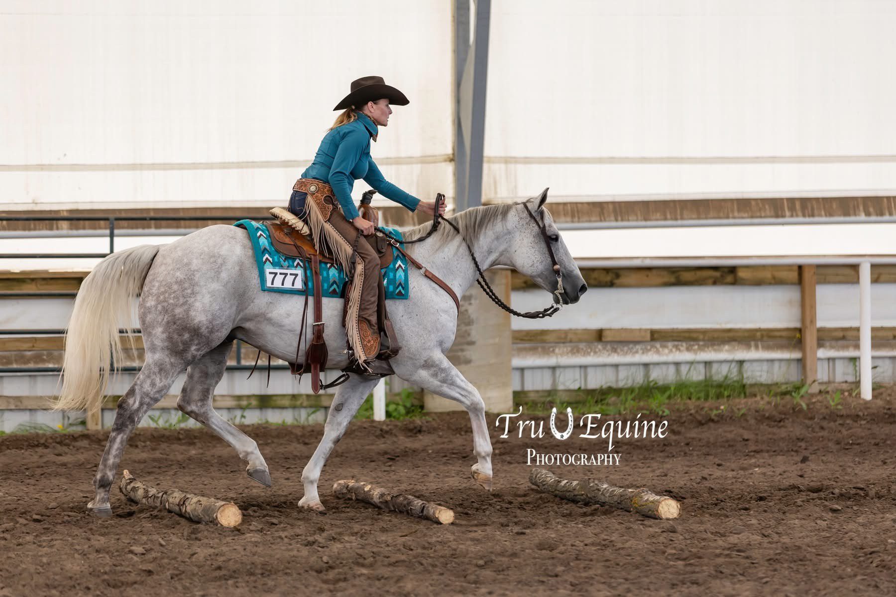 Western rider guiding gray horse over poles